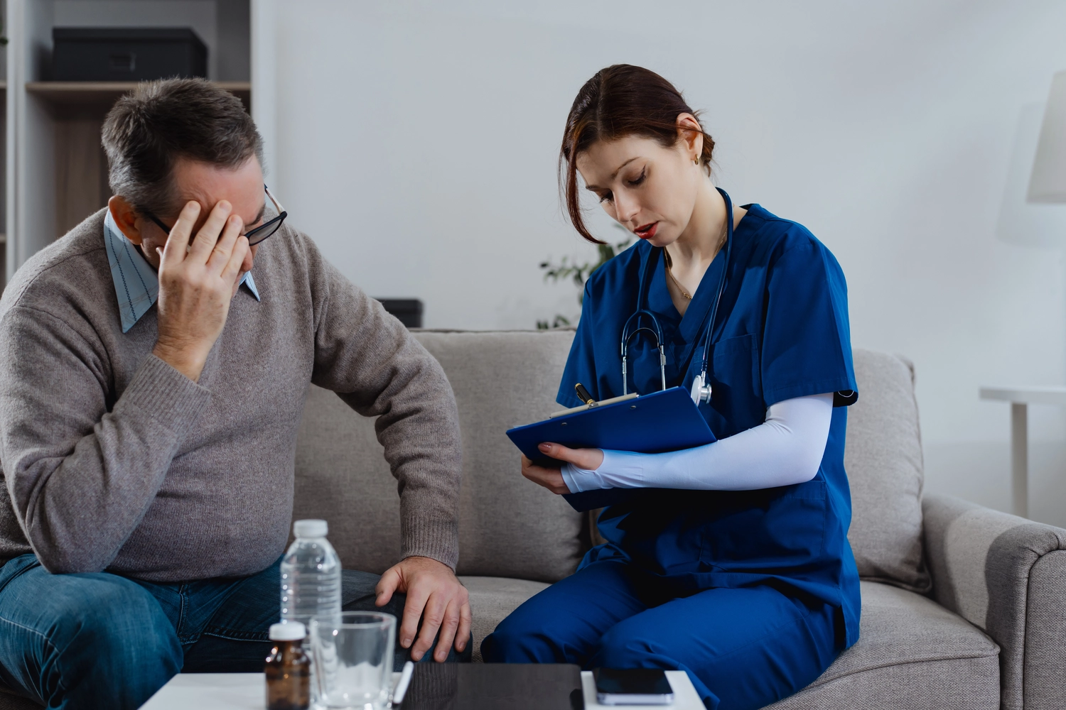 Dana Depenthal - Praxis für Logopädie - Eine junge kaukasische Krankenschwester berät einen älteren kaukasischen Mann, der auf einem Sofa sitzt, medizinisch